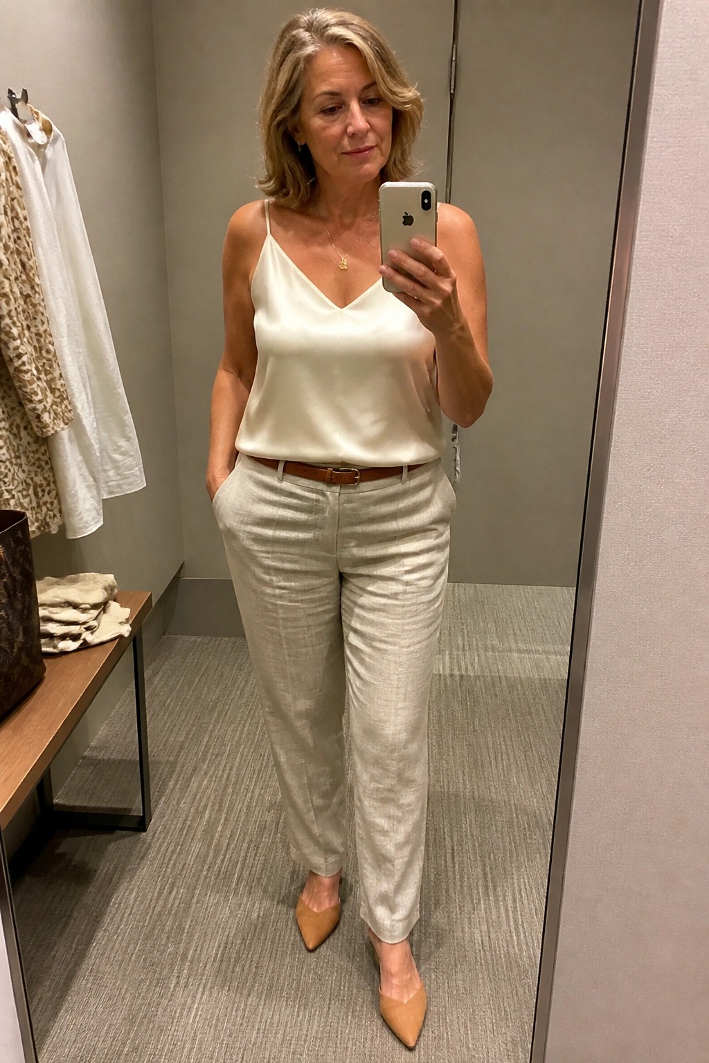 Blonde woman in ivory camisole and beige linen pants taking mirror selfie