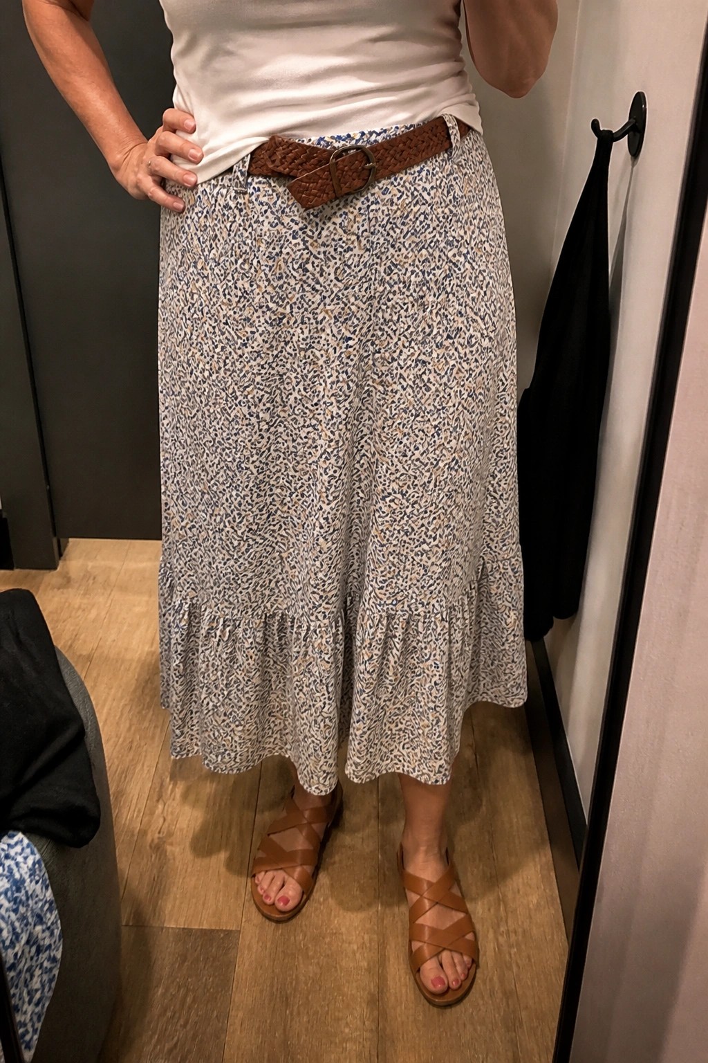 Woman in white top, long patterned skirt with ruffle, brown belt, strappy sandals