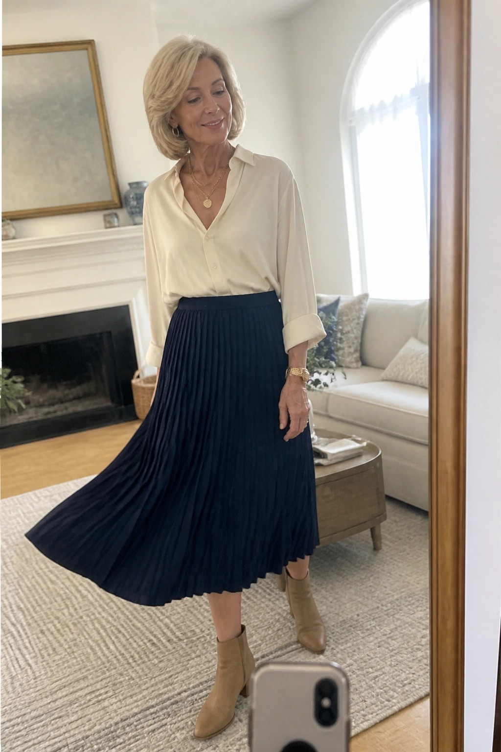Elegant woman in cream blouse and navy pleated skirt with tan boots in living room