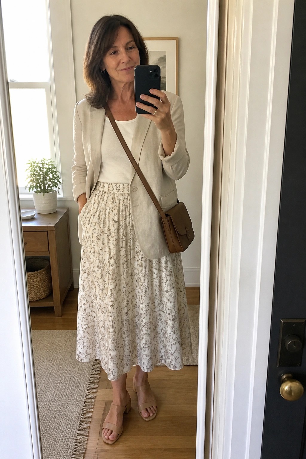 Woman in beige blazer and floral skirt taking mirror selfie with phone