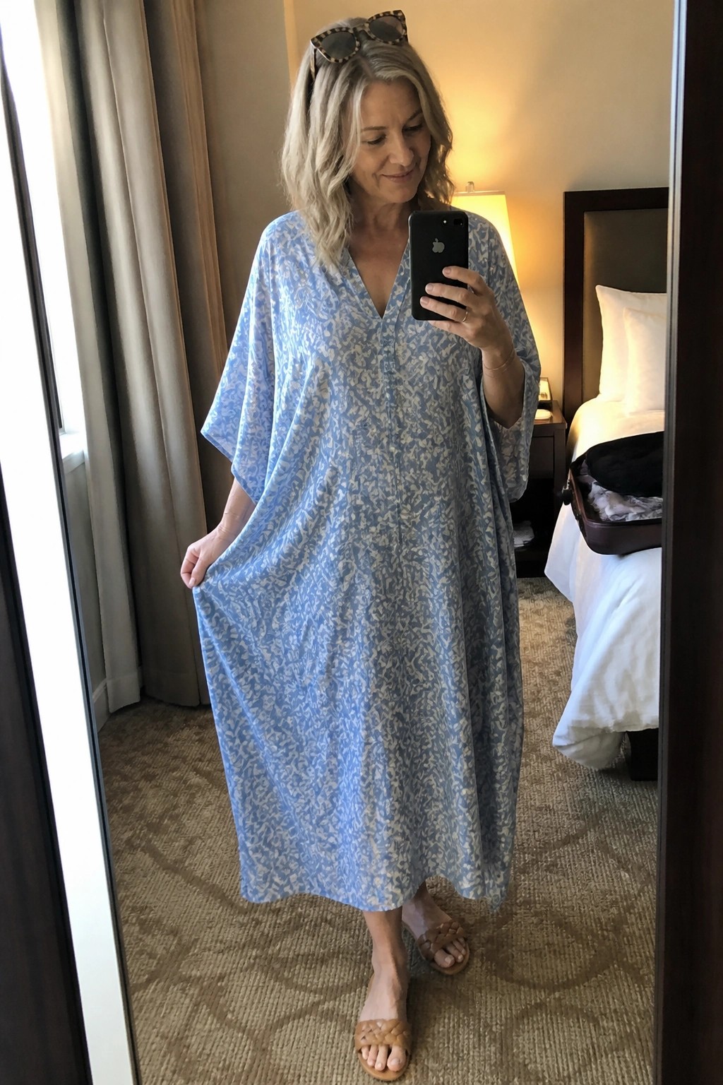 Woman in light blue patterned dress taking mirror selfie in hotel room