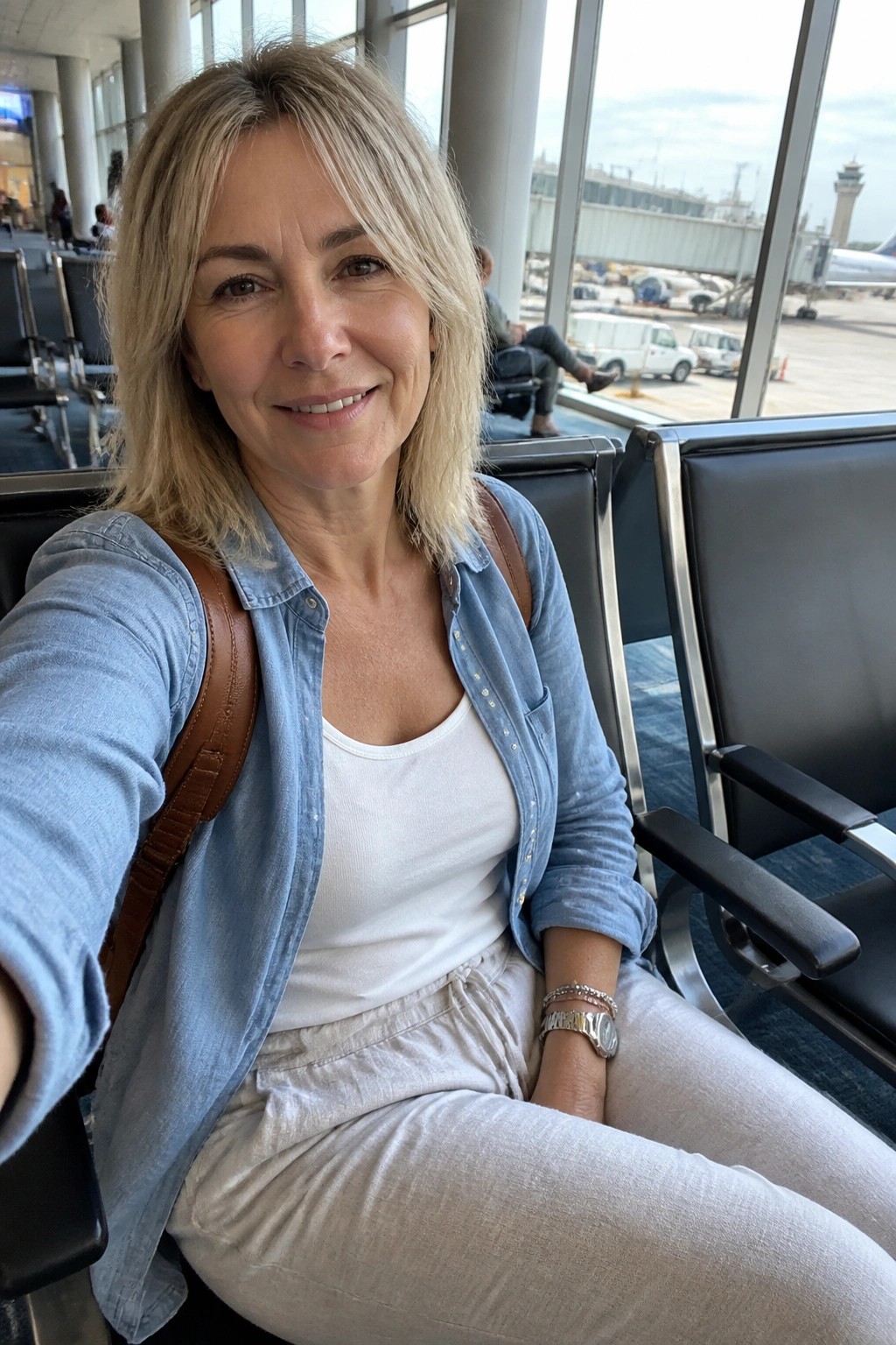 Blonde woman in denim shirt smiling for selfie in airport terminal