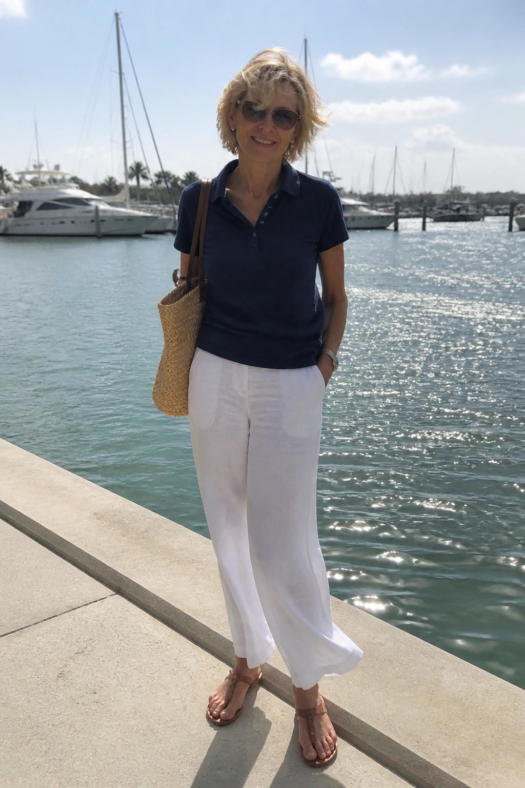 Smiling blonde woman in navy polo and white pants on sunny marina dock