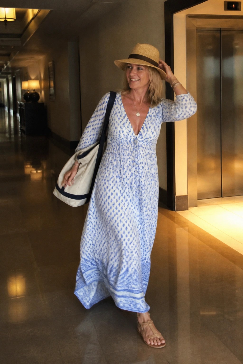 Smiling blonde woman in blue patterned maxi dress with straw hat and tote bag