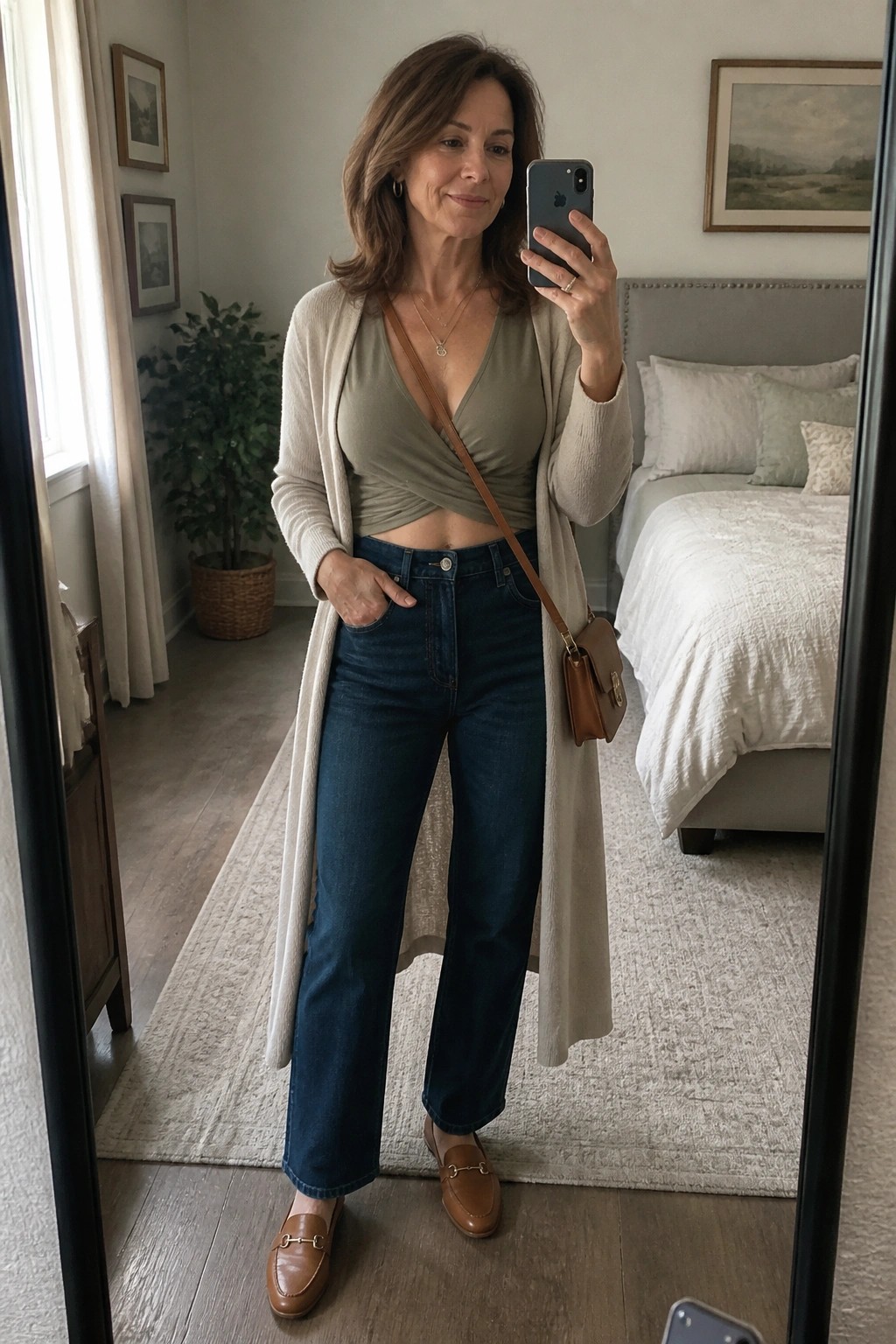Woman in beige cardigan and green wrap top taking bedroom mirror selfie.