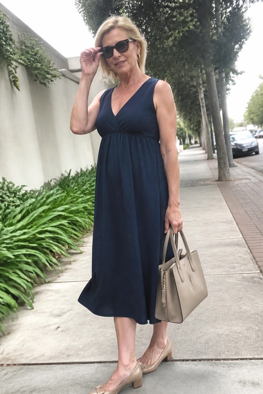 Blonde woman in navy blue dress holding beige handbag on sidewalk