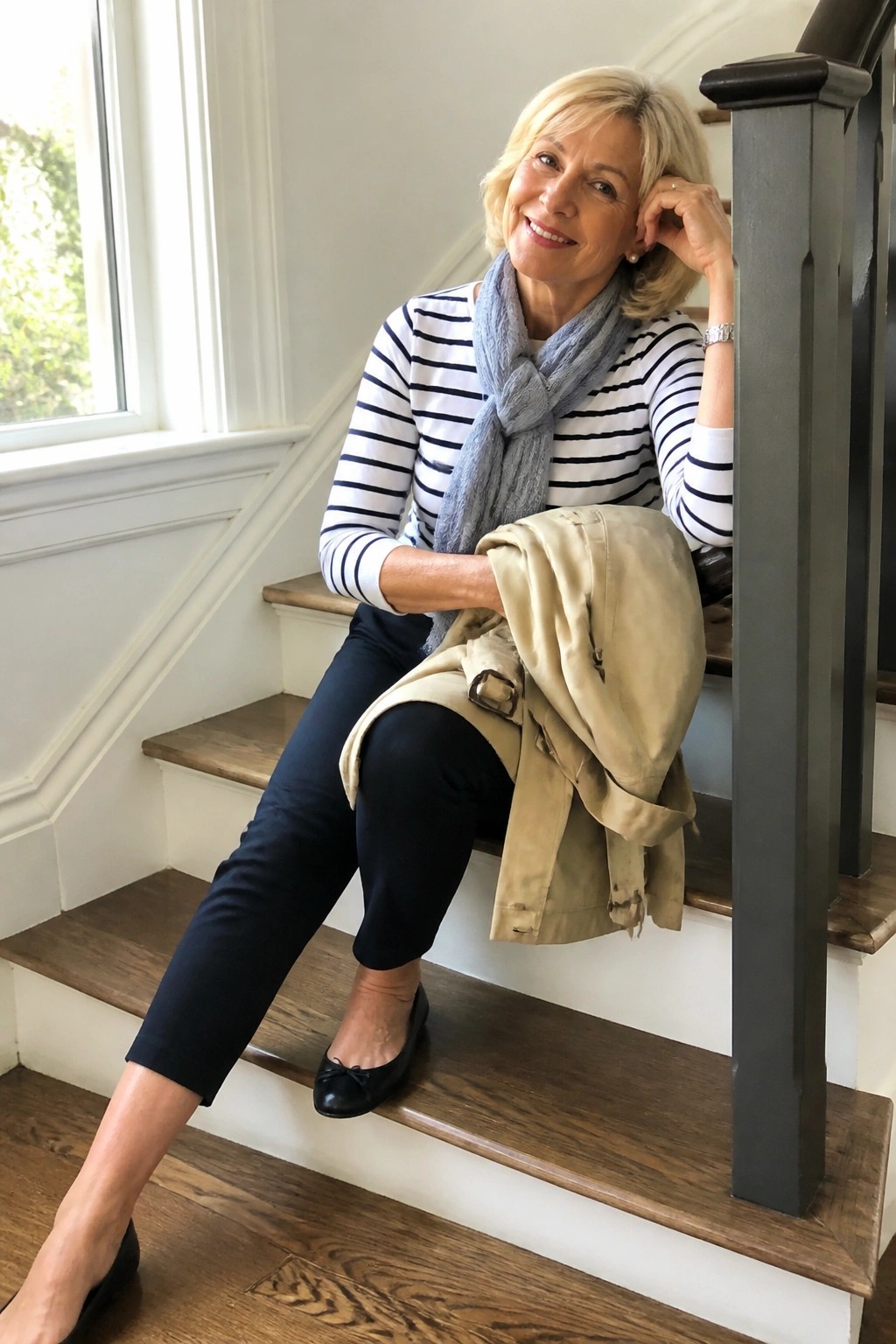 Blonde woman in striped shirt and scarf on stairs holding beige trench coat