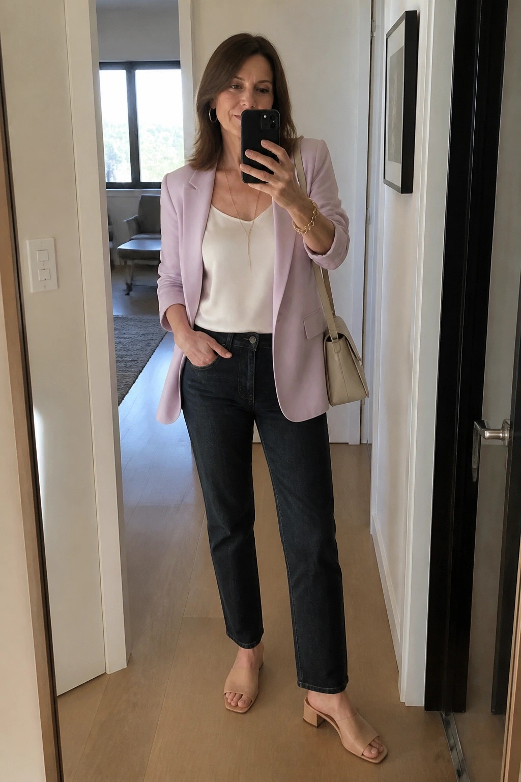Woman in lavender blazer and white top taking mirror selfie in hallway.