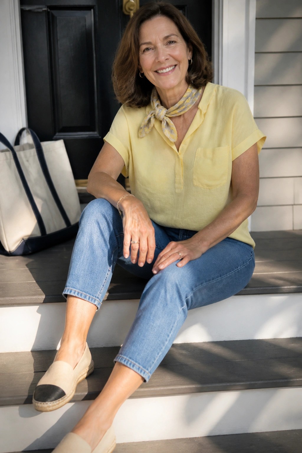 Smiling woman in yellow shirt and scarf seated on wooden porch steps with tote bag