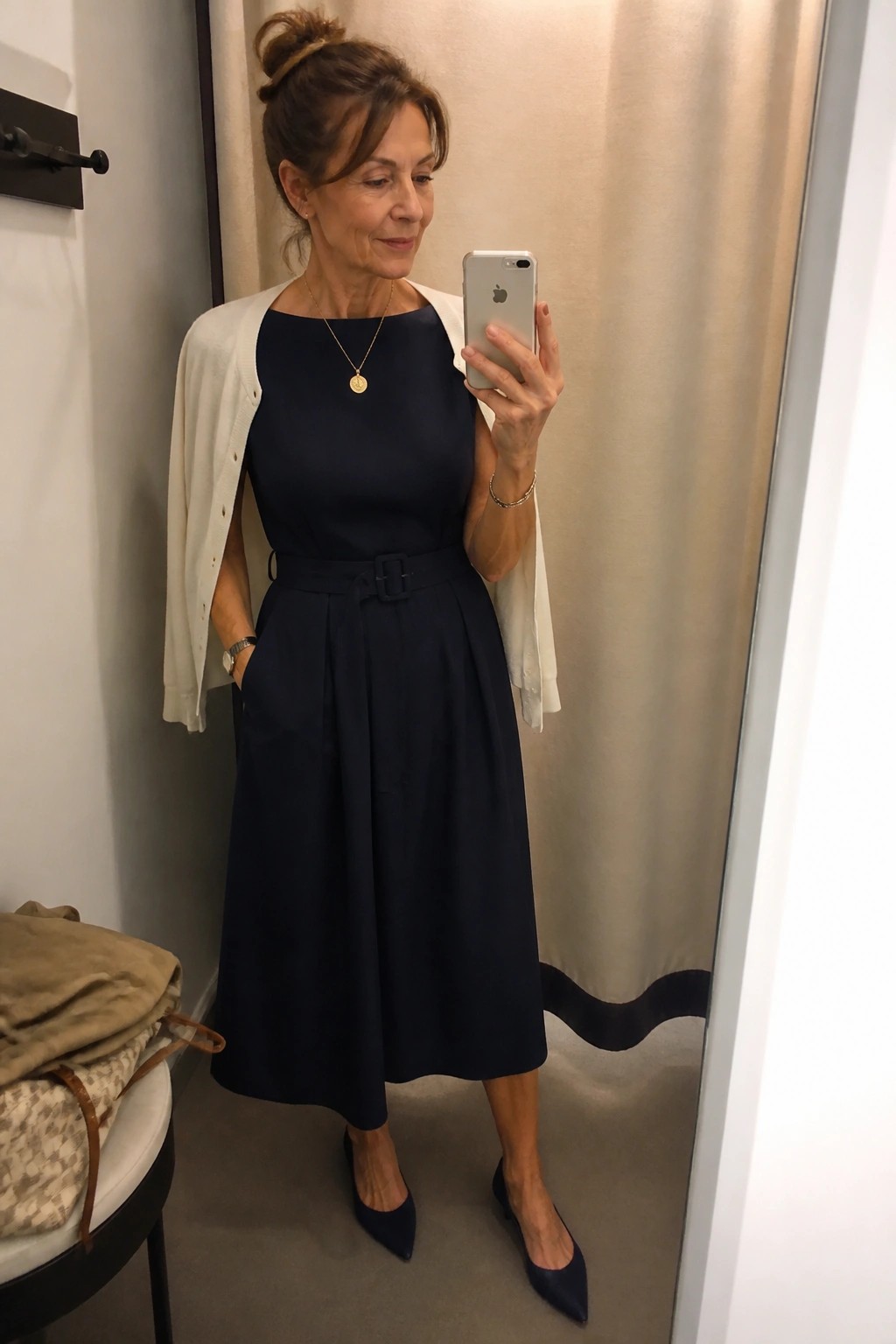 Woman in navy dress and white cardigan taking mirror selfie with phone