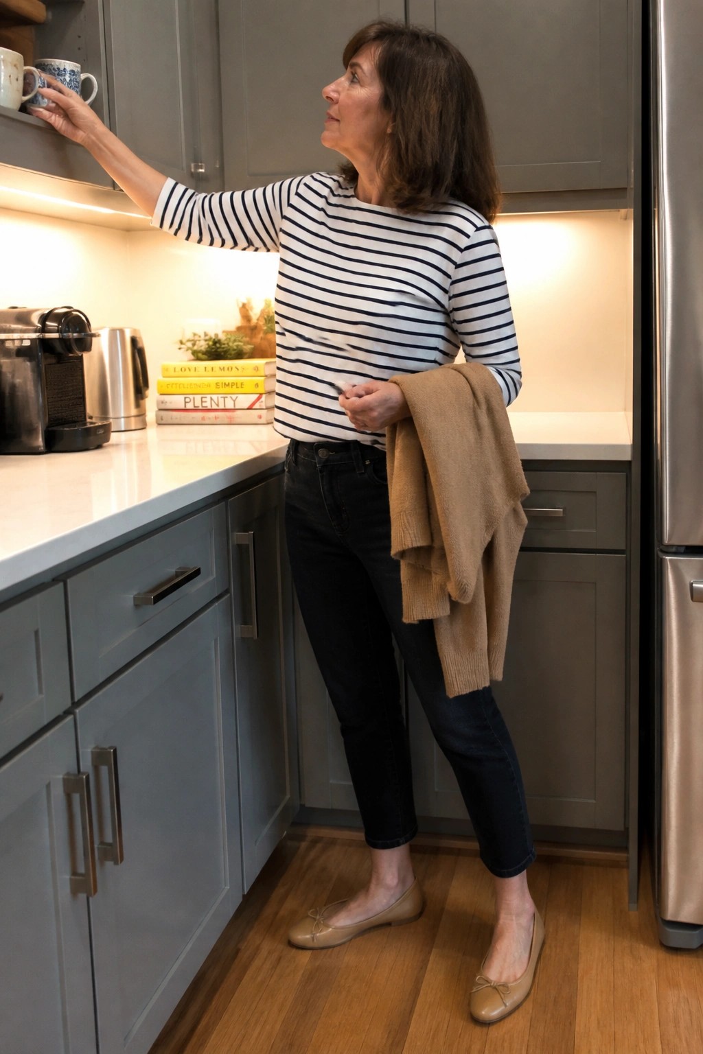 Woman in striped shirt reaches for mug while holding tan sweater in kitchen