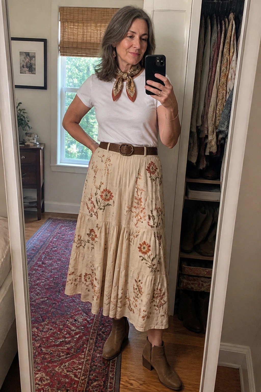 Woman in white tee and floral skirt taking mirror selfie in brown boots