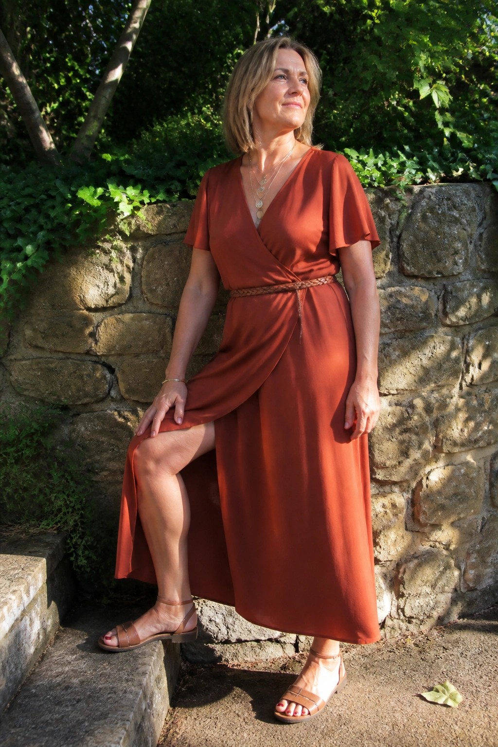 Woman in rust wrap dress posing by stone wall and steps