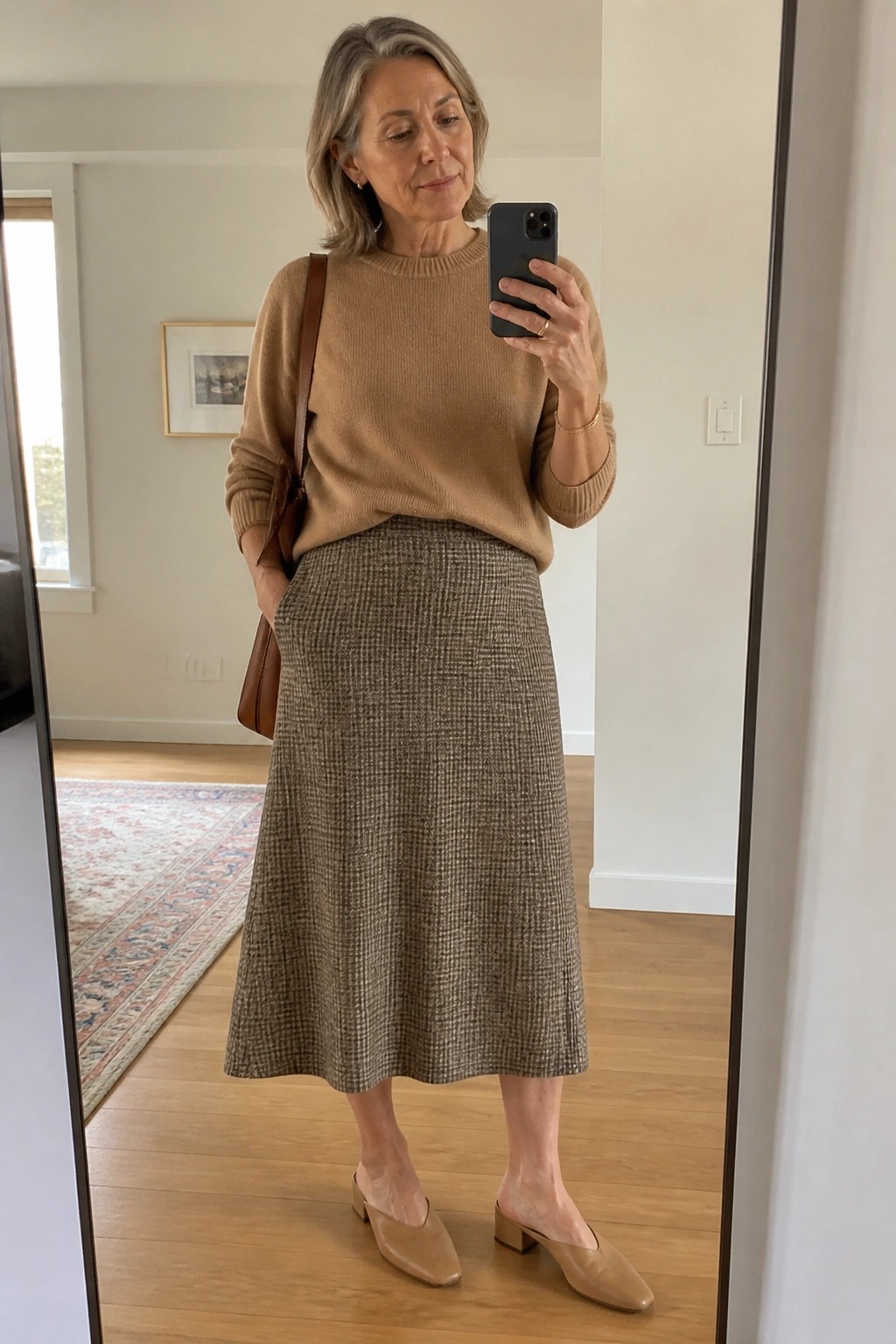 Gray-haired woman in tan sweater and checkered skirt taking mirror selfie with phone