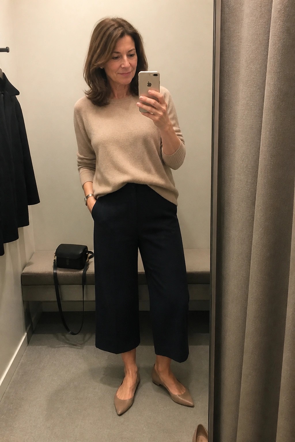 Woman in beige sweater and navy culottes taking mirror selfie in fitting room