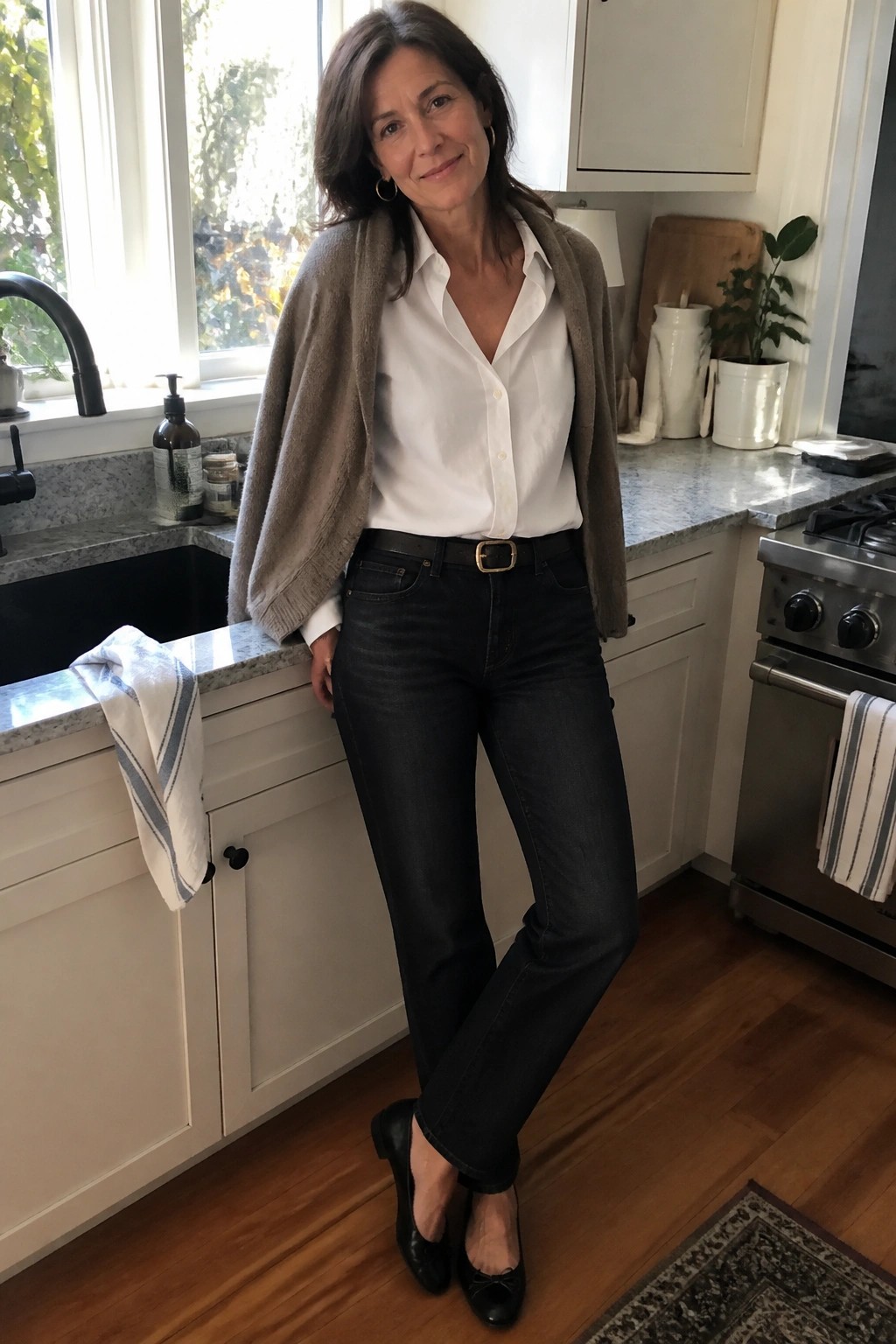 Woman in white shirt and taupe cardigan with dark jeans in bright kitchen