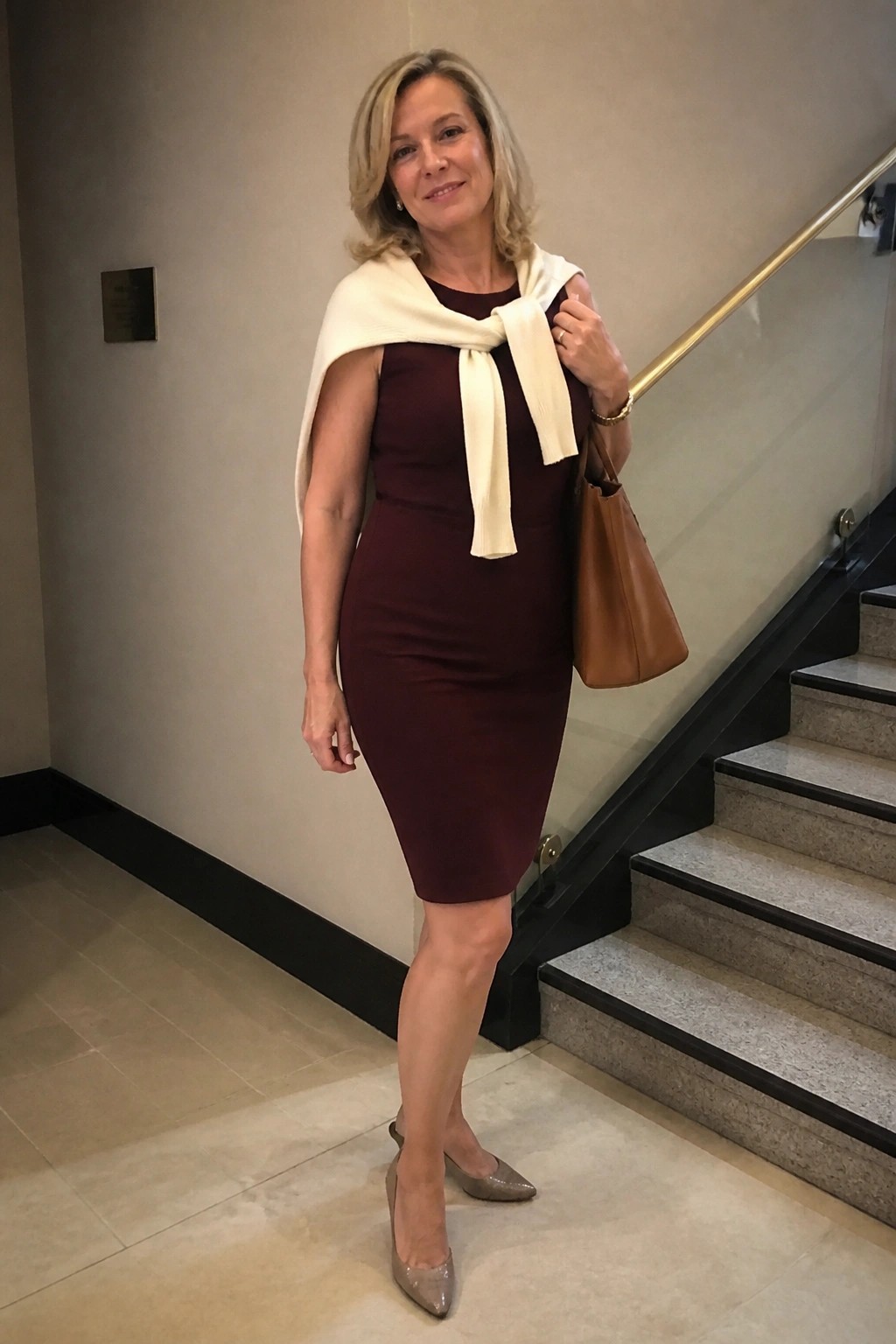Elegant woman in sleeveless maroon dress with white shawl by marble stairs