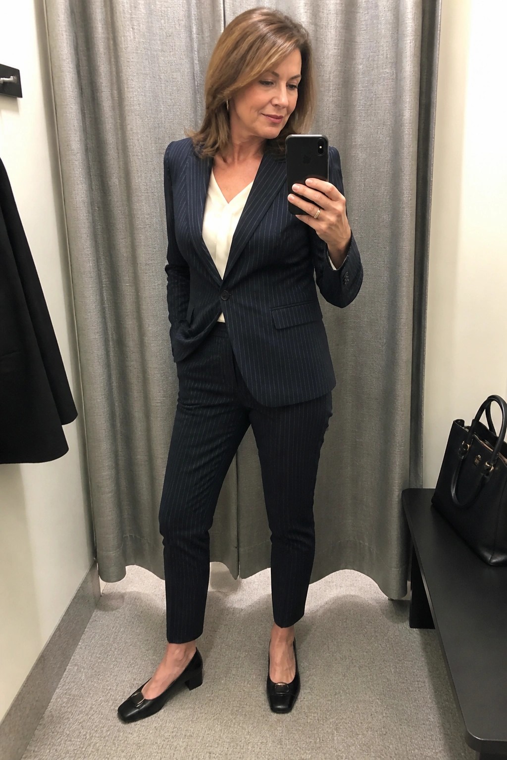 Woman in navy pinstripe suit taking mirror selfie in dressing room
