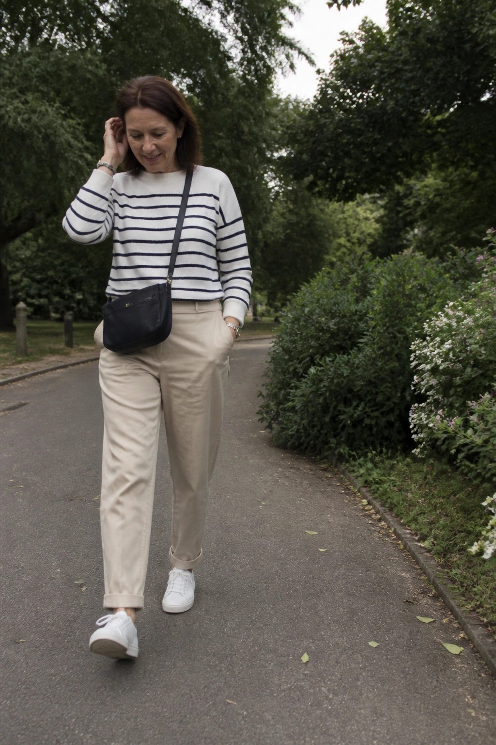 Woman in striped sweater and beige pants with black bag on park path