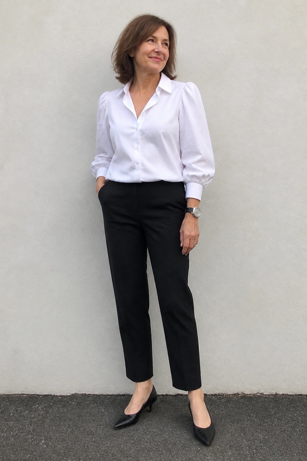 Woman in white puff-sleeve blouse and black pants standing by wall