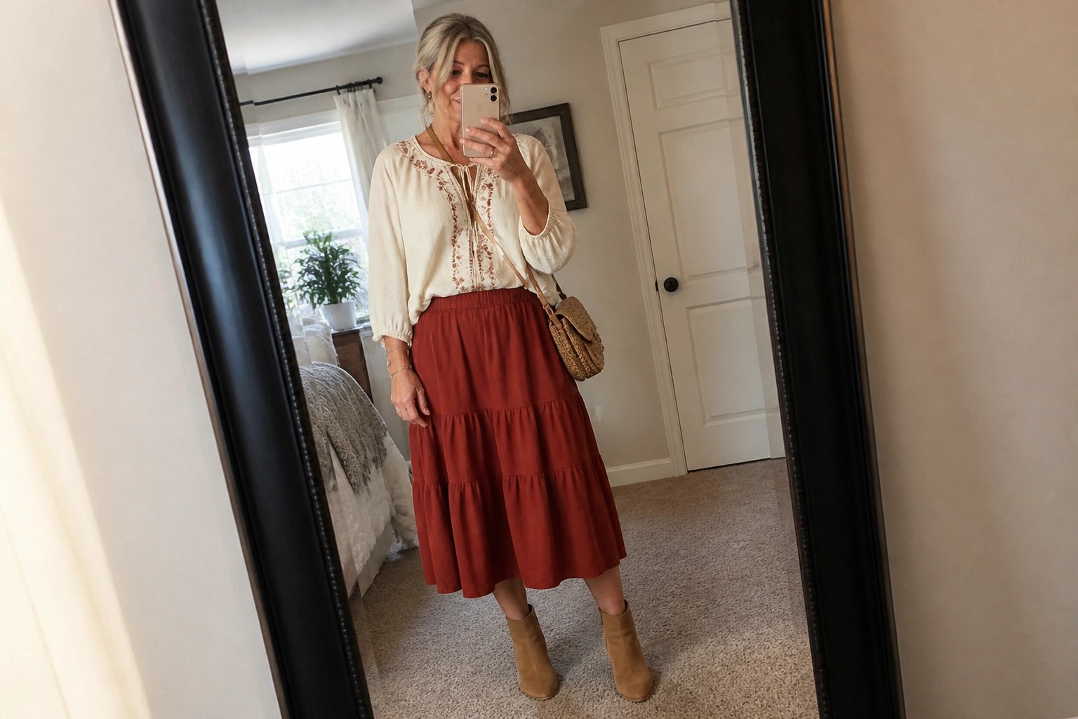 Woman in embroidered white blouse and rust tiered skirt taking bedroom mirror selfie