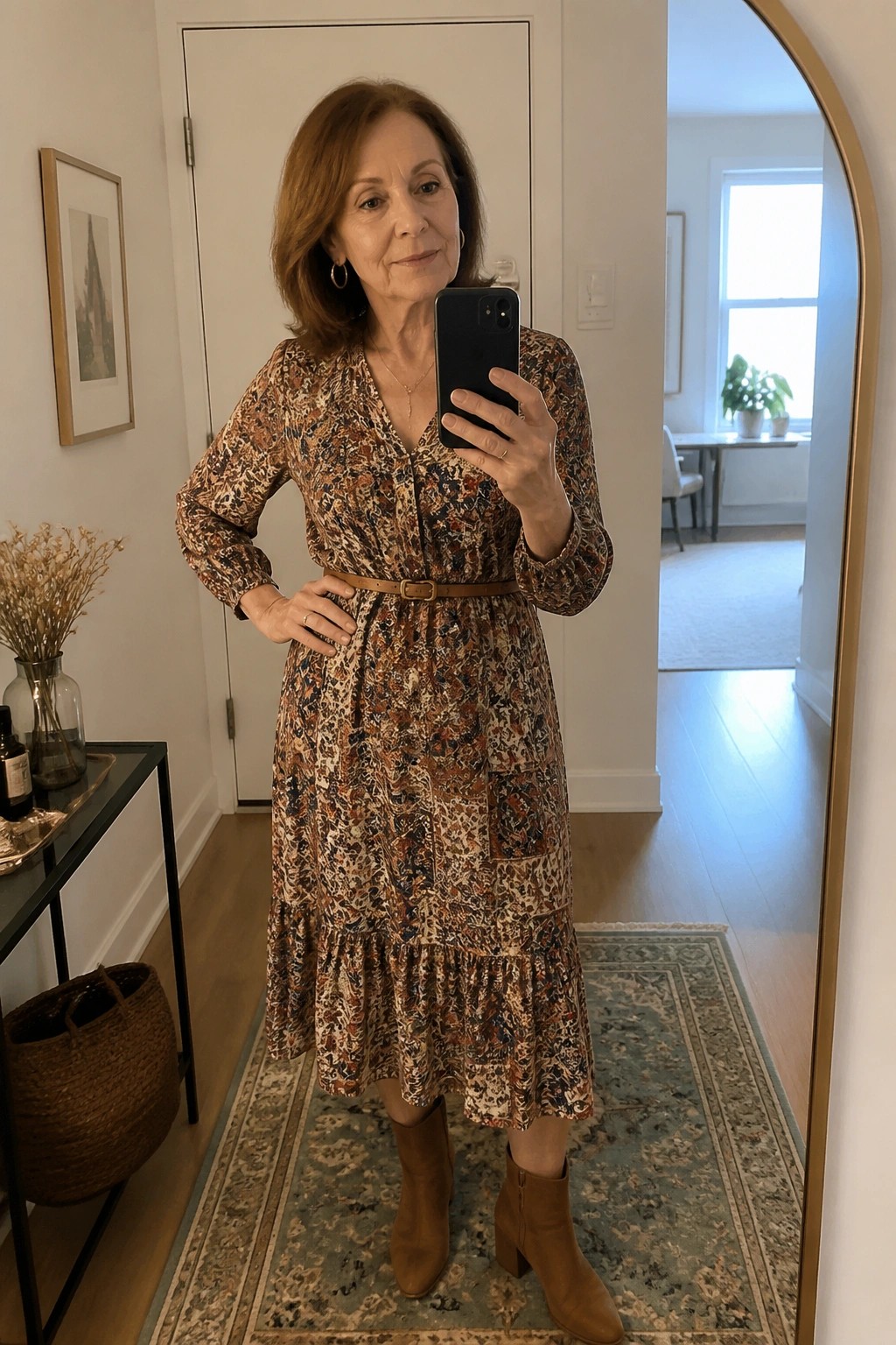 Woman in floral dress with belt and brown boots taking mirror selfie indoors