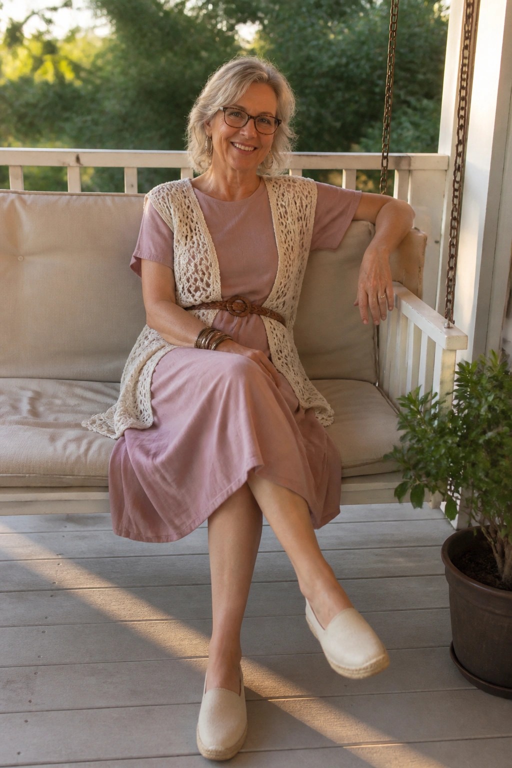 Woman over 50 in a rose midi dress layered with an open cream crochet vest, brown woven belt, beige espadrilles, and simple bracelets
