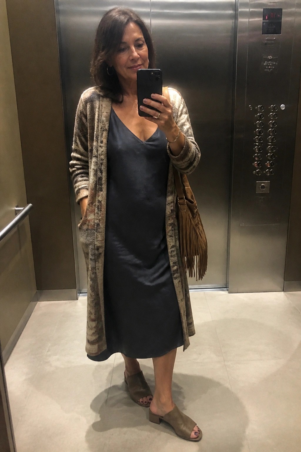 Woman in navy slip dress and patterned cardigan taking selfie in elevator