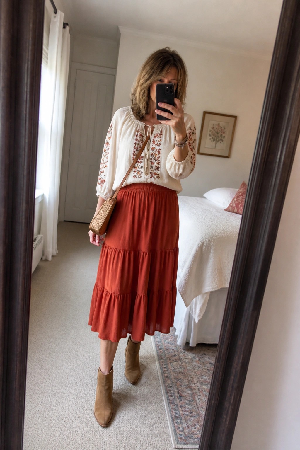 Woman in embroidered white blouse and rust tiered skirt taking bedroom mirror selfie