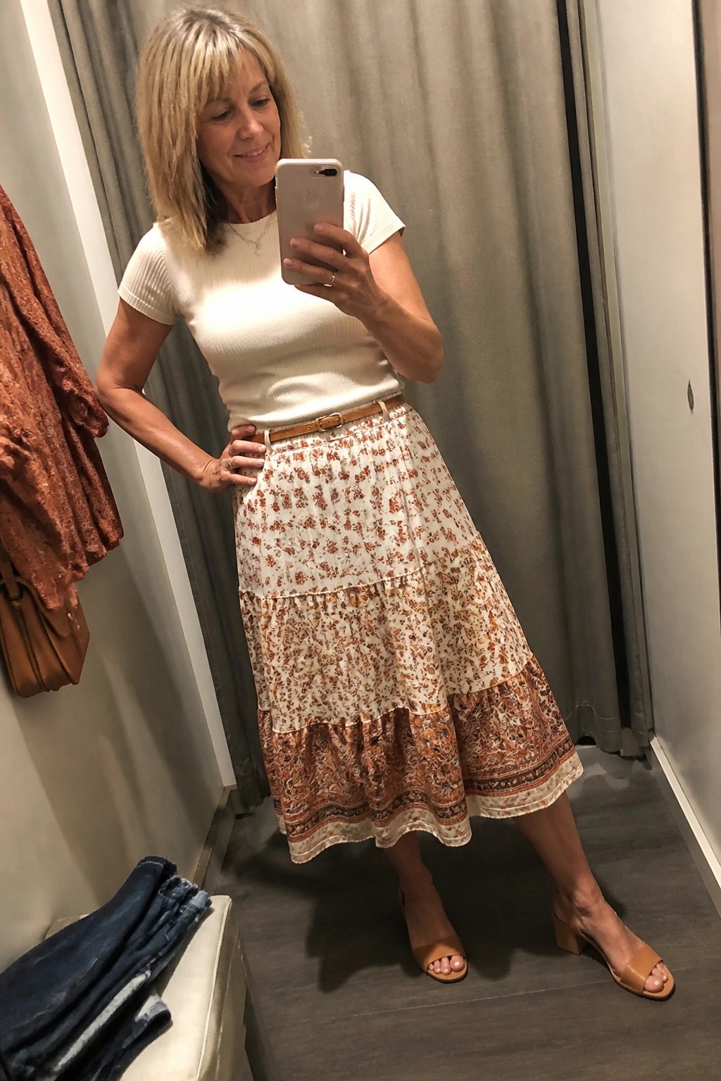 Woman in white top and floral tiered skirt taking mirror selfie in dressing room.