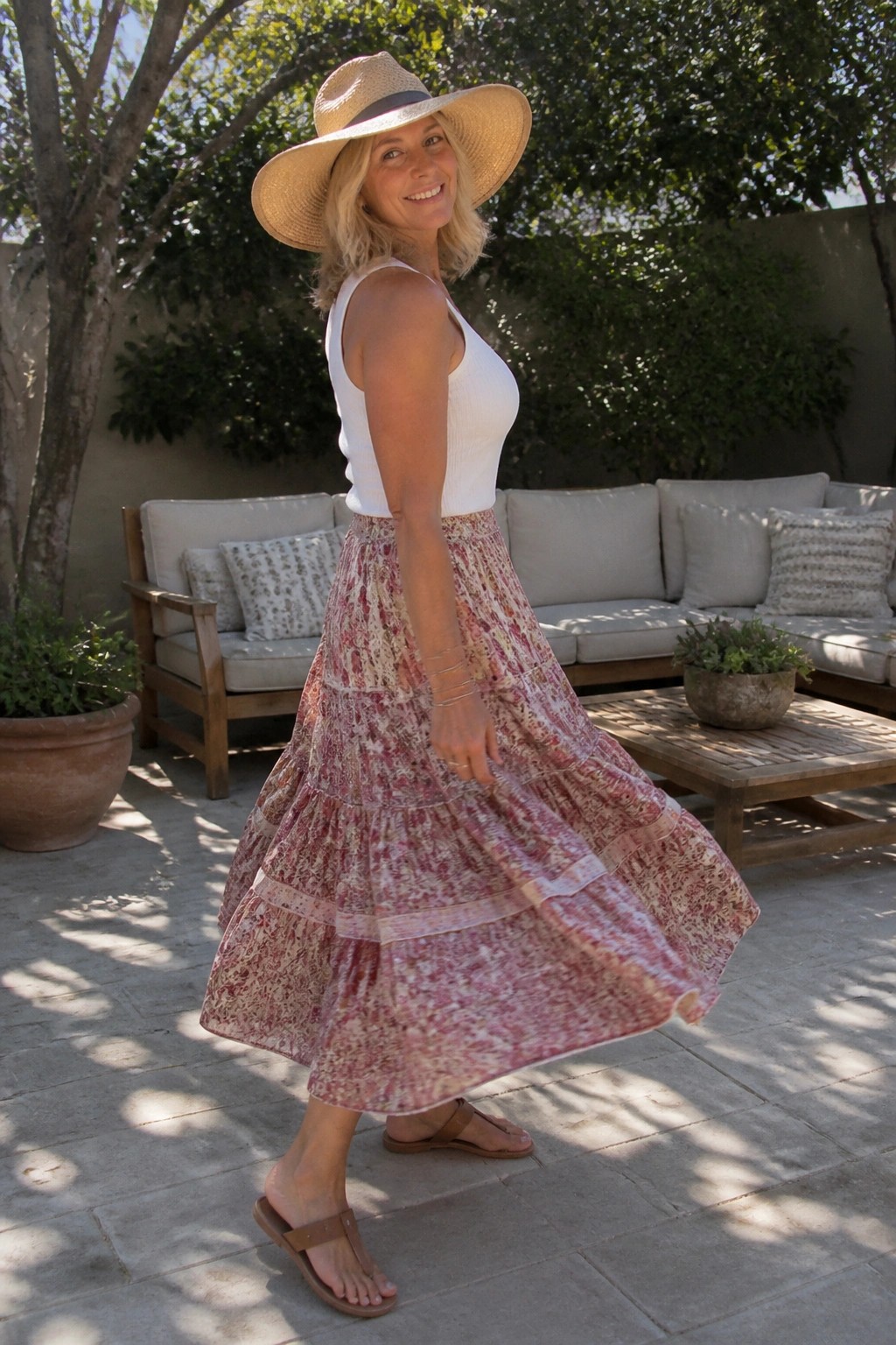 Woman in white top and floral tiered skirt with straw hat on sunny patio