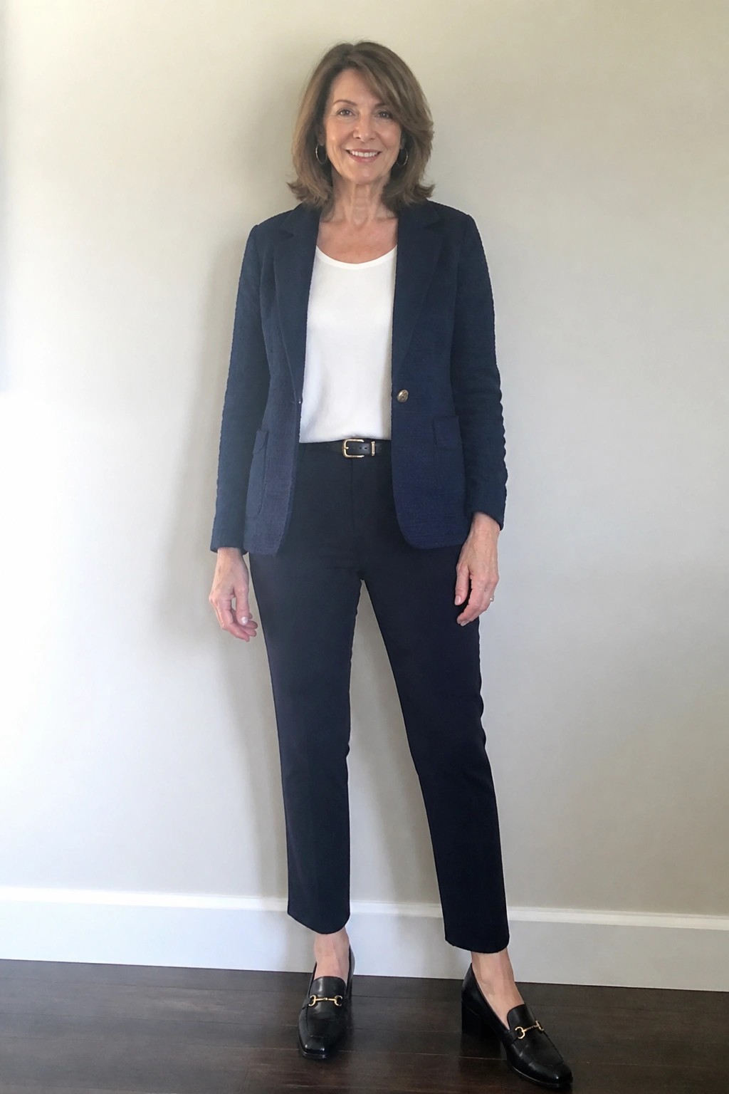 Smiling woman in navy blazer over white top with dark pants and loafers.