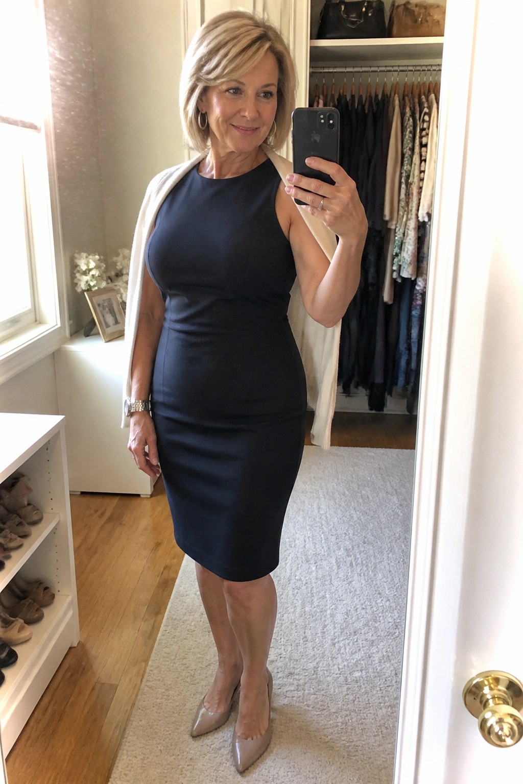 Woman in navy dress with white shawl taking mirror selfie in closet