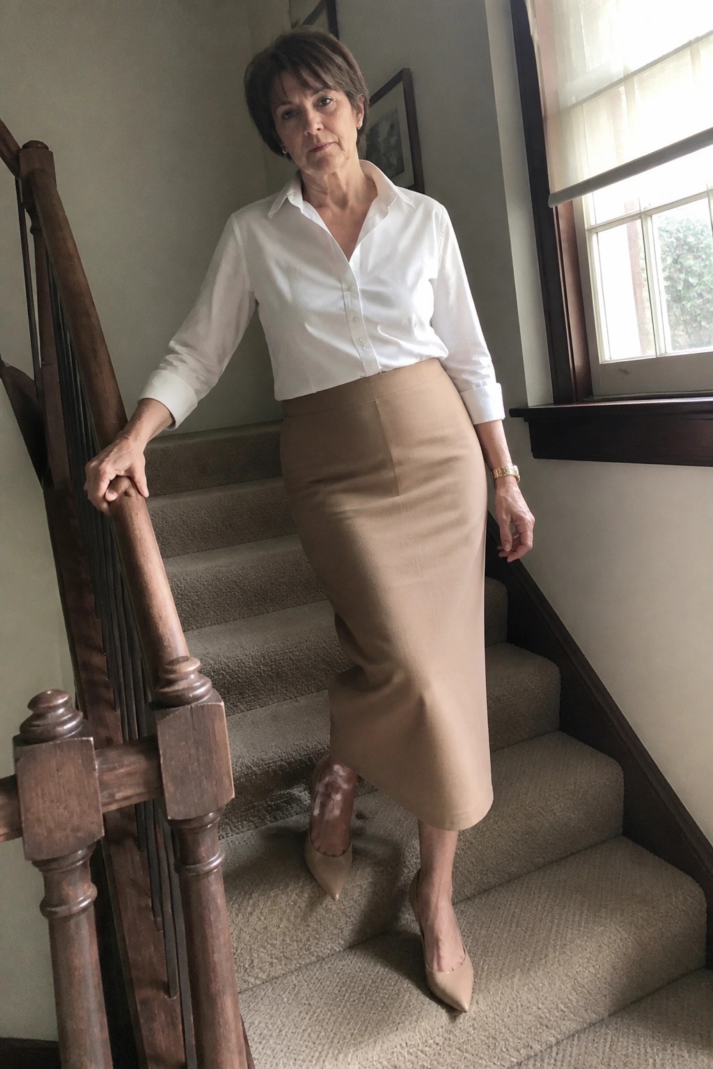 Woman in white shirt and beige skirt standing on carpeted staircase holding railing