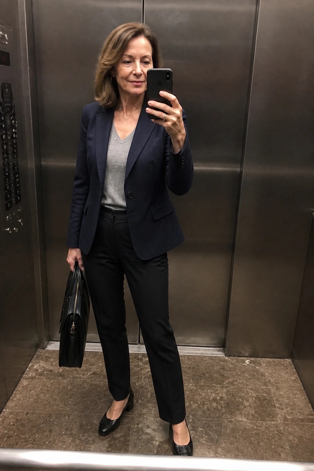 Woman in navy blazer and black pants taking selfie in elevator