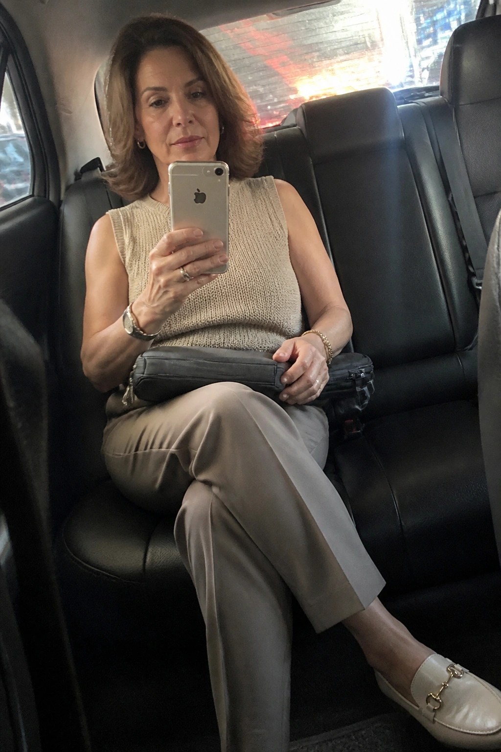 Woman in beige top holding iPhone in black leather car seat
