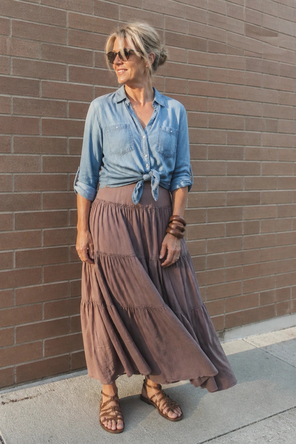 Woman in tied blue denim shirt and tiered mauve skirt by brick wall