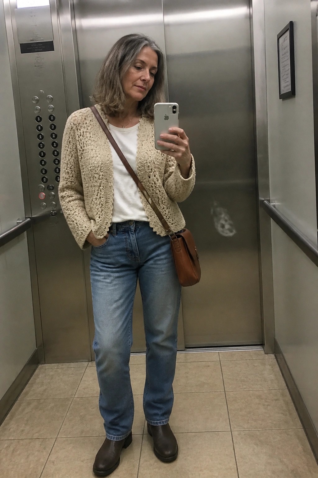Woman with graying hair in cream crocheted cardigan takes selfie in elevator