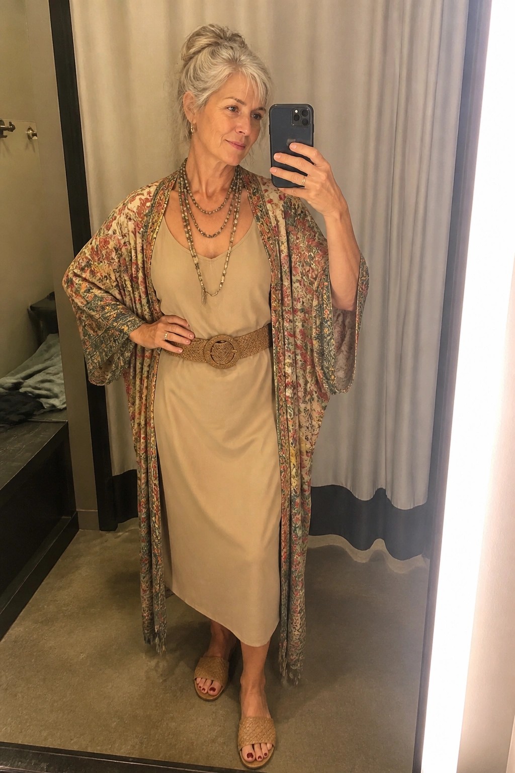 Gray-haired woman in beige dress, floral kimono, and wide belt takes mirror selfie.