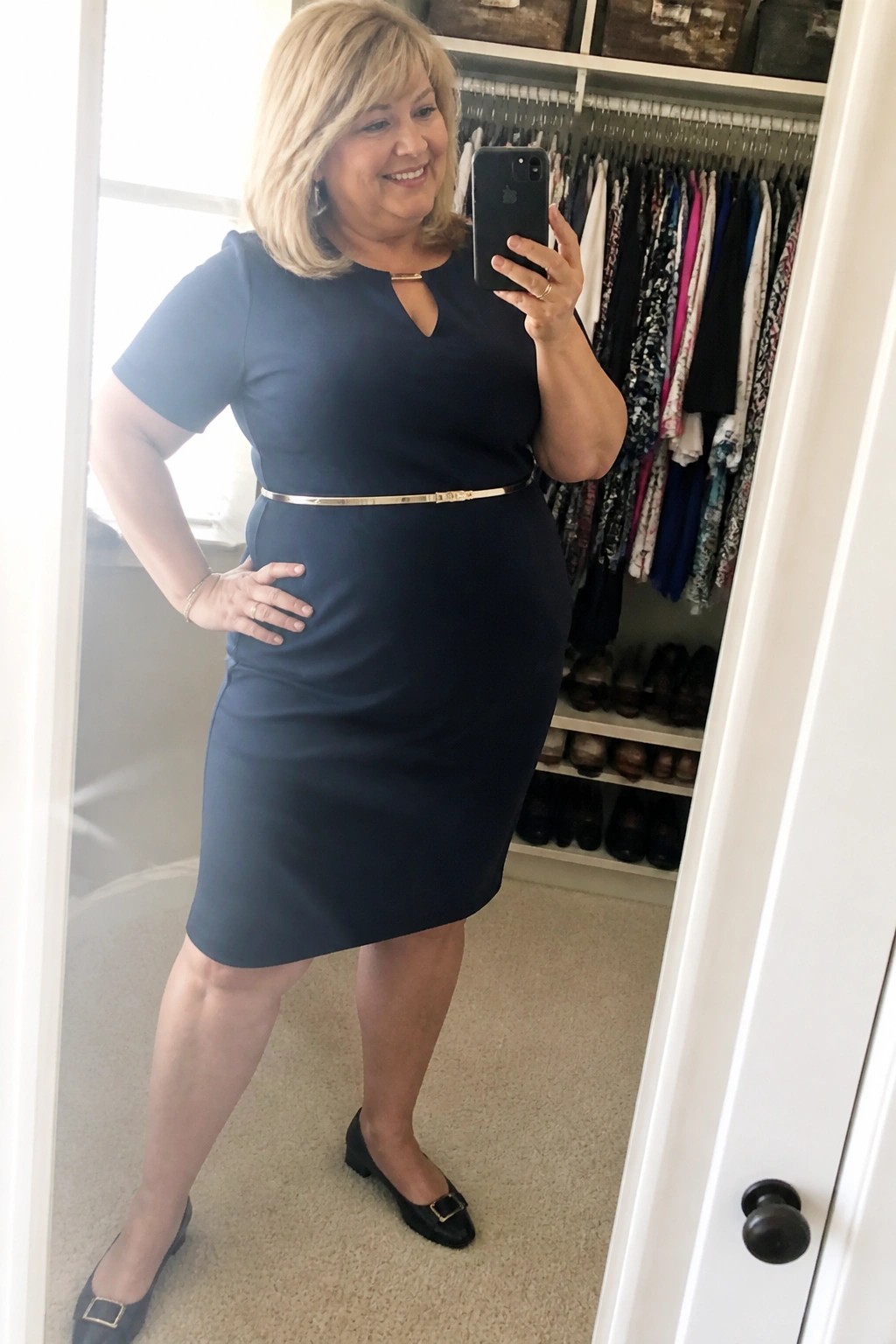 Woman in navy blue dress with gold belt taking closet mirror selfie