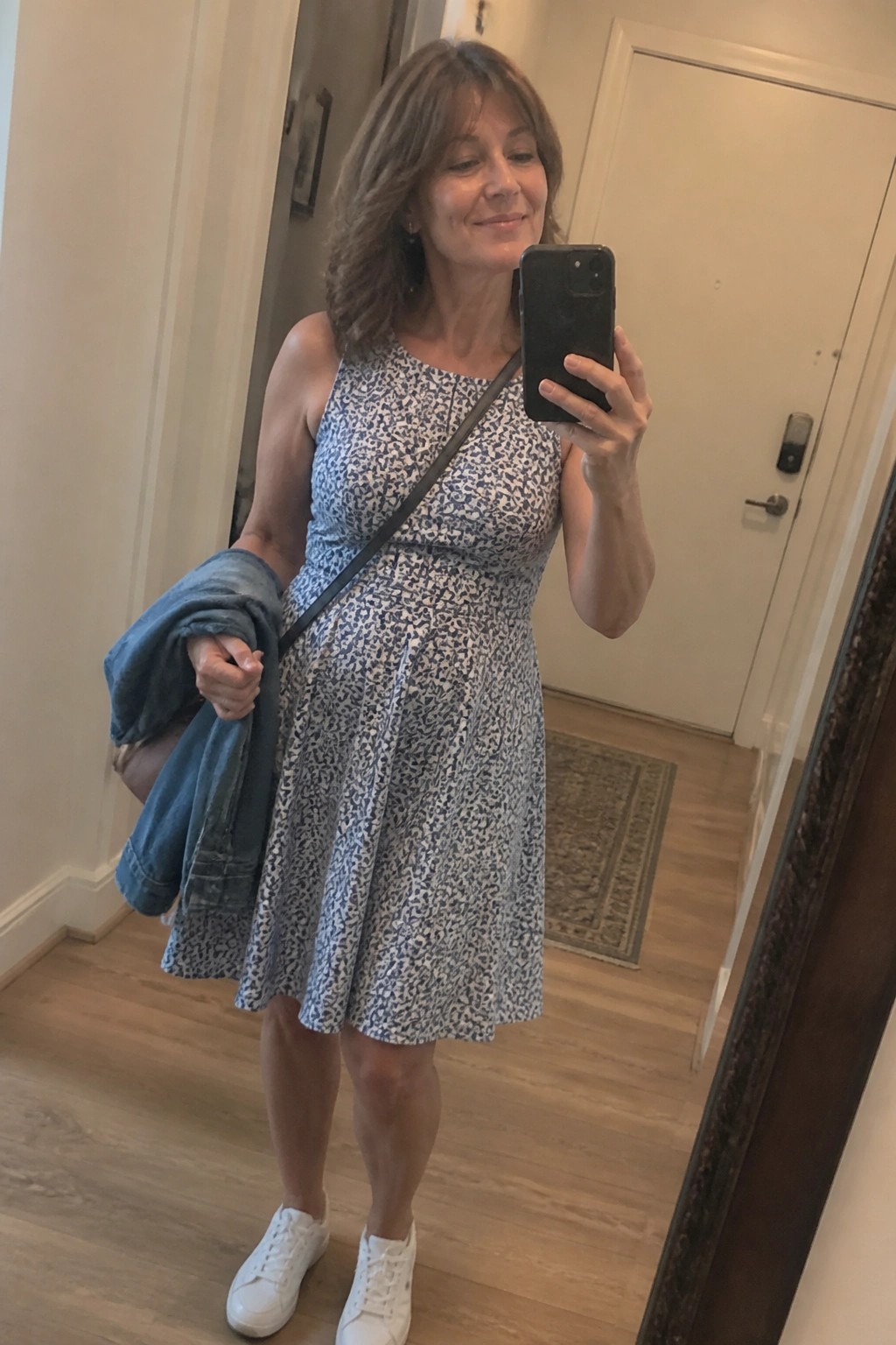 Woman in blue patterned dress takes mirror selfie holding denim jacket