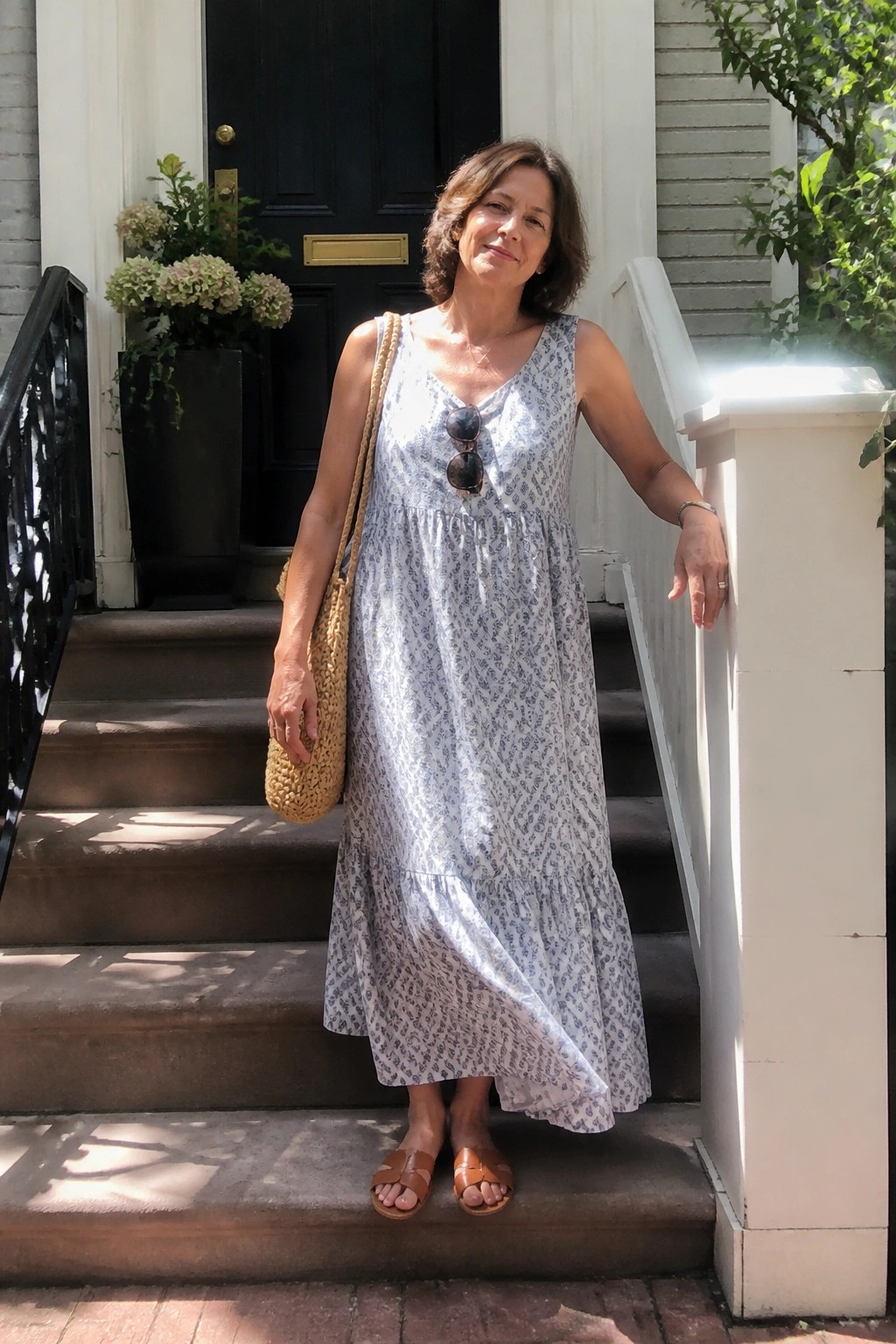 Woman in blue patterned sundress holding woven bag on front steps