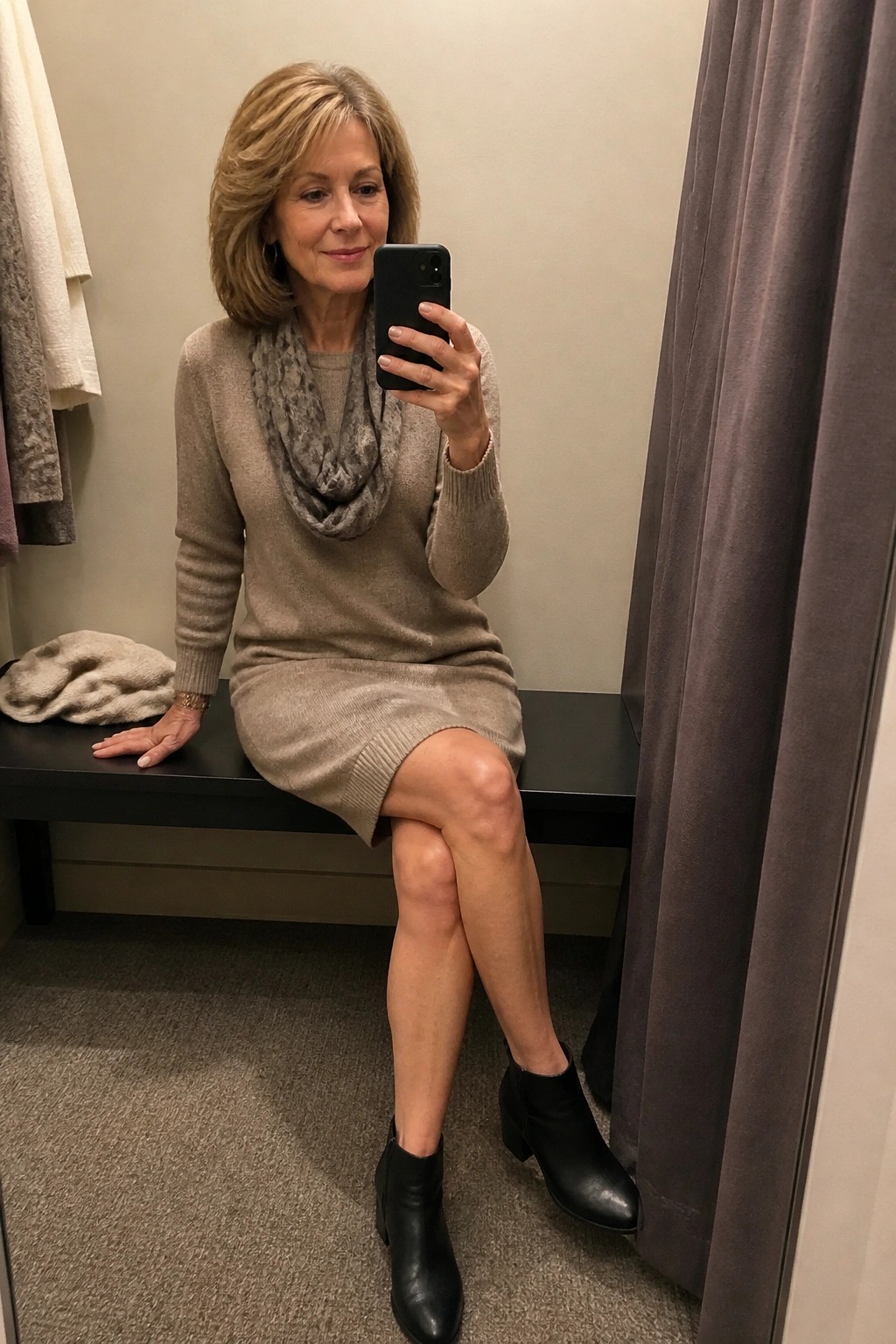 Woman in beige sweater dress and black boots takes mirror selfie on bench