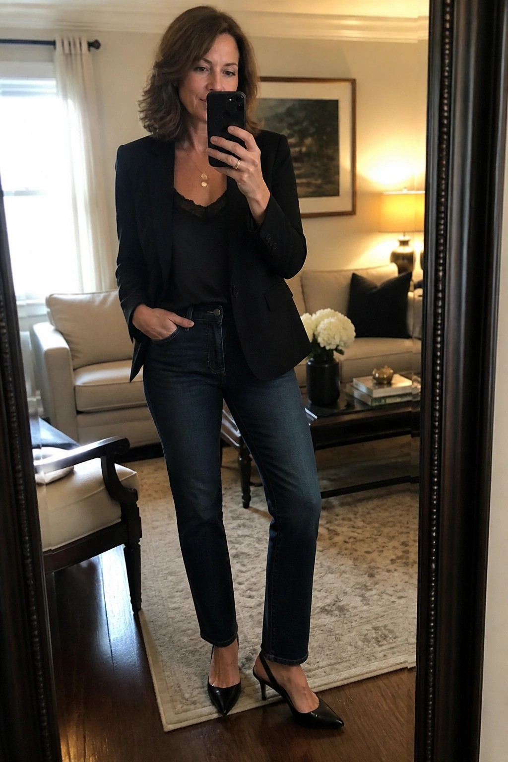 Woman in black blazer and jeans taking mirror selfie in living room