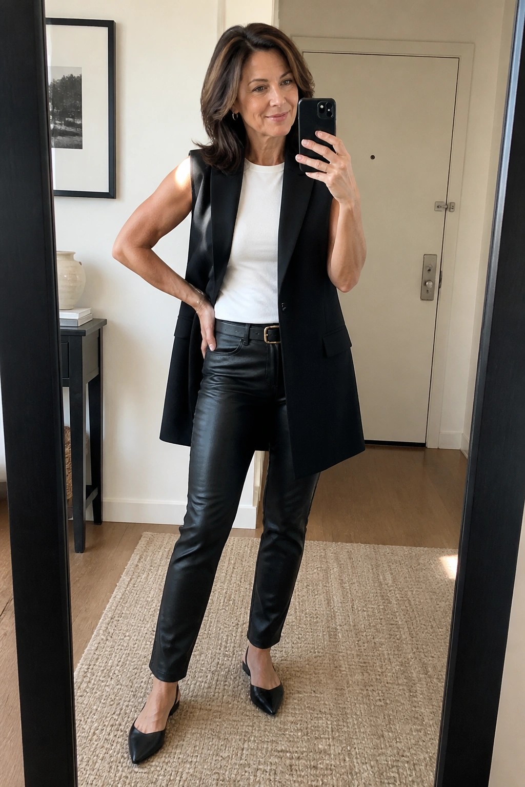 Woman in black vest and leather pants taking mirror selfie with phone