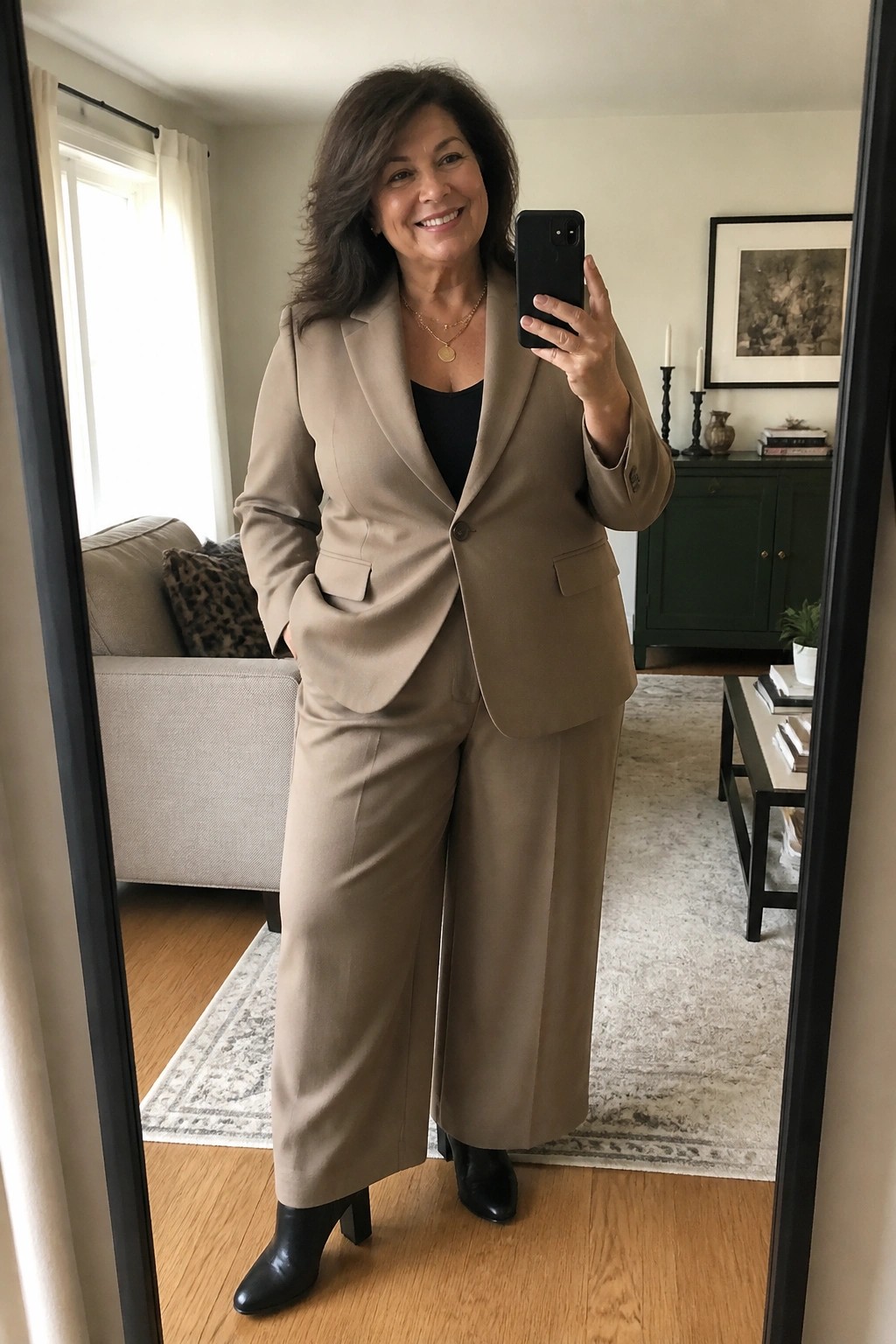 Smiling woman in beige pantsuit takes mirror selfie in living room