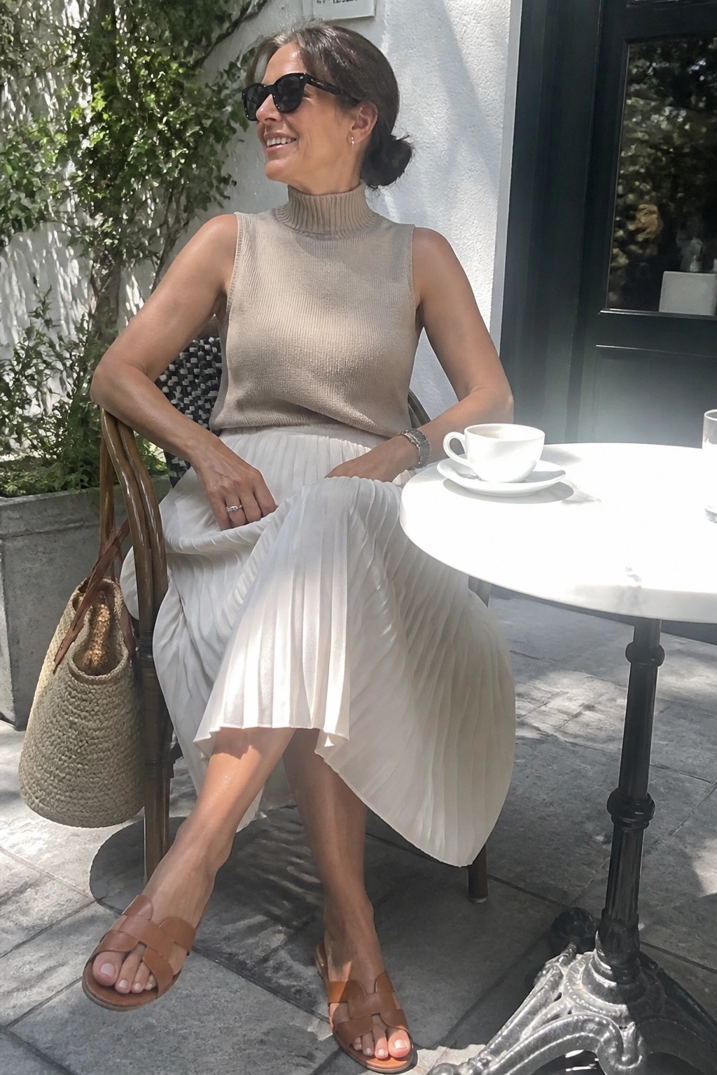 Woman in beige sleeveless turtleneck and white pleated skirt at outdoor cafe table