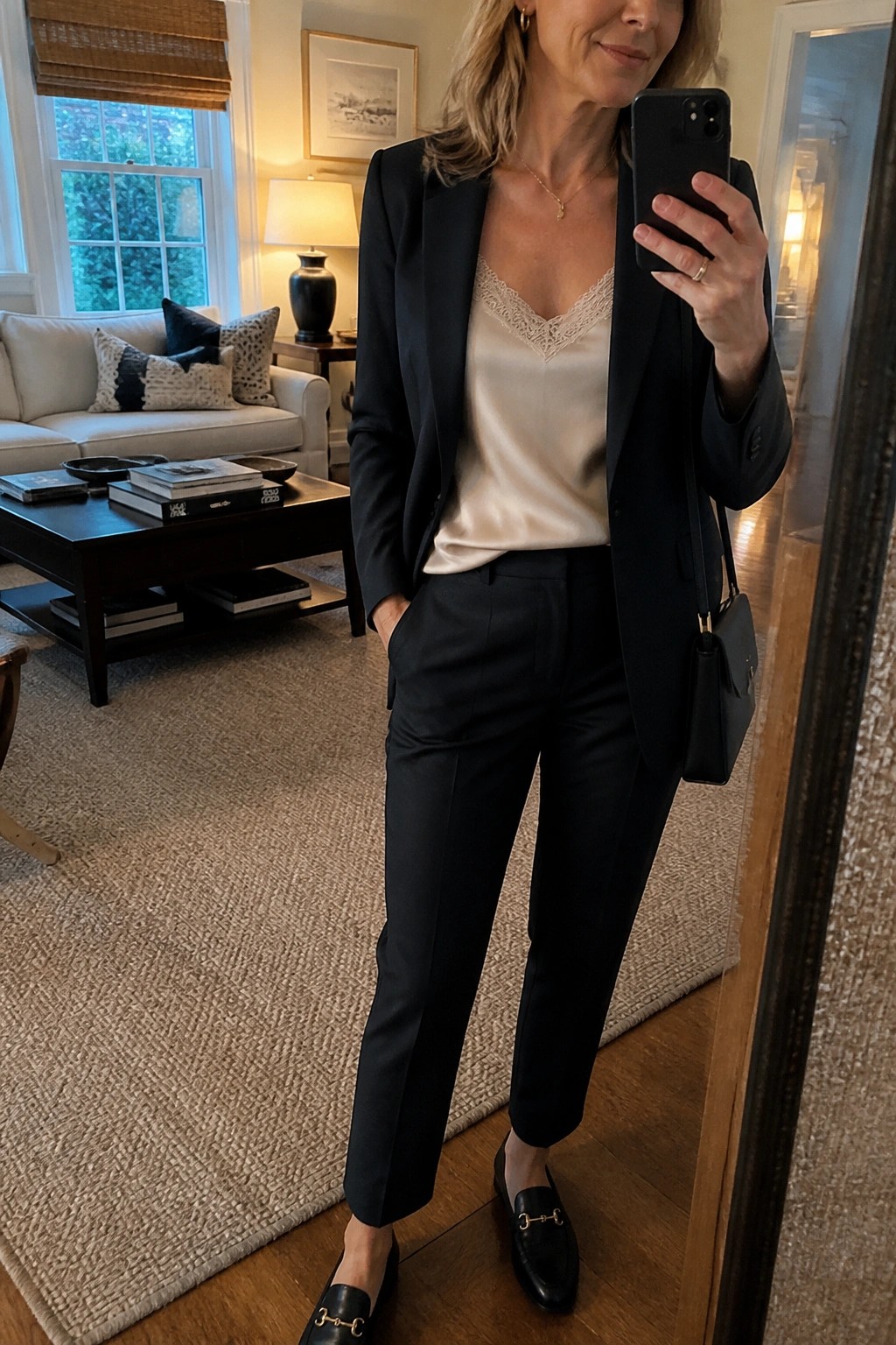 Woman in black blazer and beige satin camisole taking mirror selfie in living room