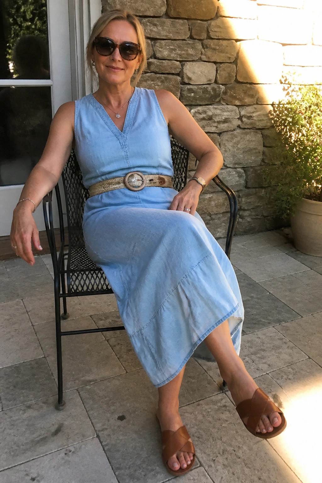 Woman in light blue denim dress with belt seated on sunny patio