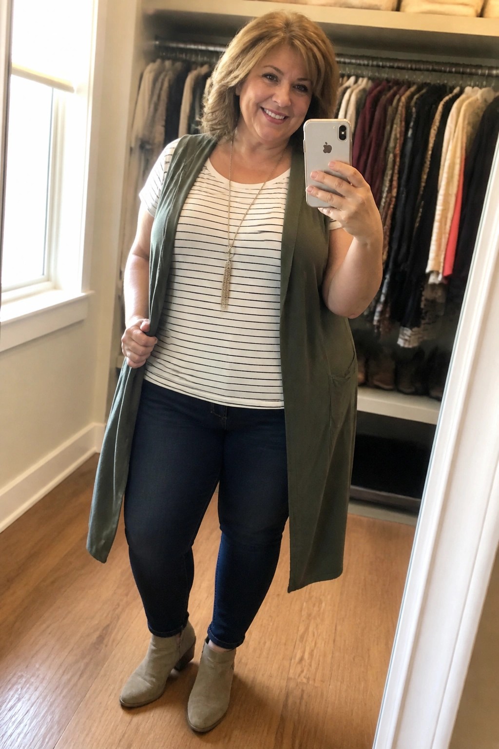 Woman in striped top and green vest taking mirror selfie in closet